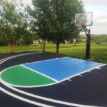 Full-color custom basketball court striping completed by Davis Line Striping for a residential property. Custom-painted backyard basketball court with blue and green zones