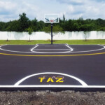 Custom full-court basketball striping with yellow arc and “TAZ” logo painted by Davis Line Striping. Custom outdoor basketball court with yellow arc and personalized lettering